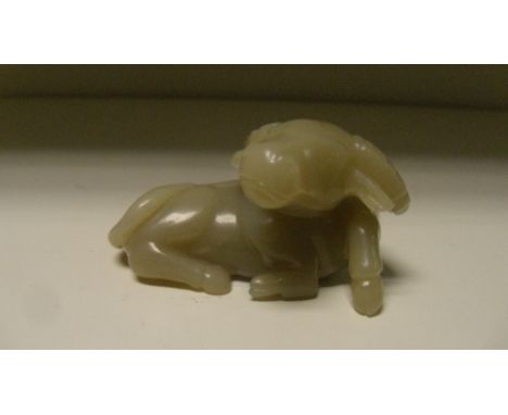 A pale grey jade buffalo carved with one leg raised from its recumbent position, the stone with brown inclusions, 6.5cm (2.5 