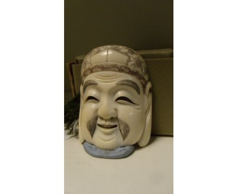 An ivory mask netsuke of Ebisu, signed Deme Tamatoshi, he wears a brocaded cap and smiles, the two ends of his moustache stai