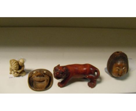 Three netsuke and a wooden tiger, one of the former carved as a smiling face, 5cm (2 in) high, another carved from a nut kern