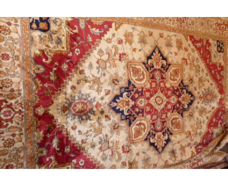 A Heriz style carpet with central floral medallion on a beige ground contained by many borders. 280cm X 200cm