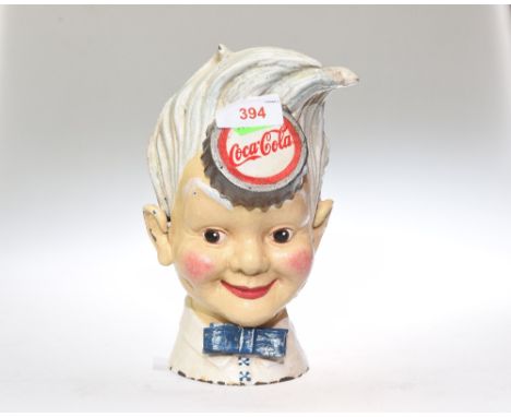 A novelty Coca-Cola cold painted money box in the form of a blond haired boy with  blue bow tie with a coca-cola bottle top s