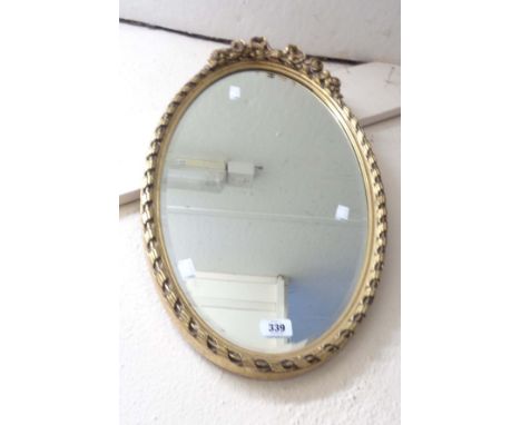 A vintage gilt framed bevelled oval wall mirror with bow and floral decoration to top