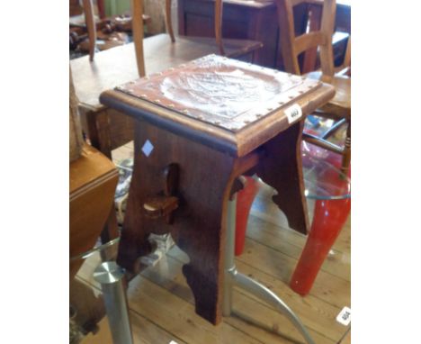 An old stained oak framed stool with studded tooled leather seat panel, set on shaped standard ends with pegged stretcher
