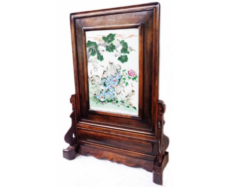 An antique Chinese hardwood table screen and carved stand, inset with a porcelain panel decorated in the famille rose palette