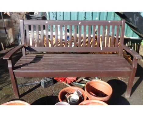 A teak three seater garden bench with slatted seat and back and brown stained finish