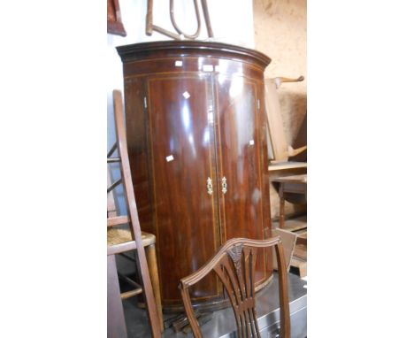 A 74cm antique mahogany and strung wall mounted bow front corner cabinet with shelves enclosed by a pair of doors