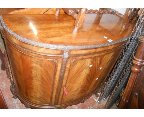 A 1.17m 1920's flame mahogany and crossbanded bow front sideboard with carved decoration and shelves enclosed by a cupboard d