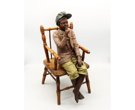 A 20th century painted plaster figure of a boy wearing a peaked cap in a seated position, upon a wooden bamboo miniature chai