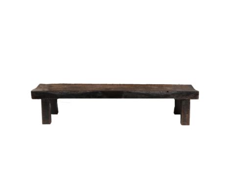 A PRIMITIVE OAK LOW BENCH. the solid plank top raised on square section supports, 193cm wide, 45cm deep  Provenance; By reput