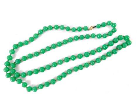 A string of jade coloured glass beads,  on a knotted string strand, with yellow metal clasp, stamped 9ct, 90cm long, 109.1g a