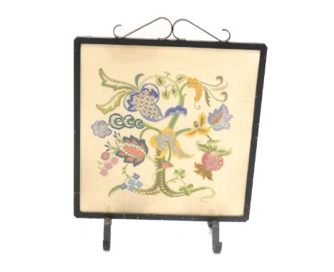 A 20thC iron framed fire screen, with floral embroidered centre, on scroll feet, 63cm high, 47cm wide, 19cm deep. 