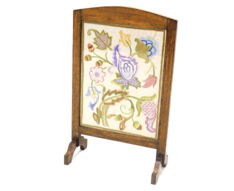 An early 20thC oak framed fire screen, with embroidered floral centre, on scroll feet, 75cm high, 43cm wide, 22cm deep. 