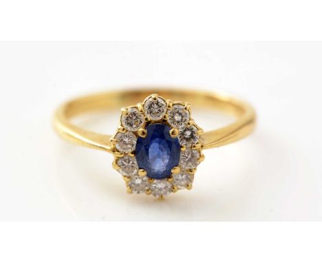 A sapphire and diamond cluster ring, the oval facet cut sapphire measuring 5.6 x 4.5 x 2.8mm, surrounded by ten brilliant cut