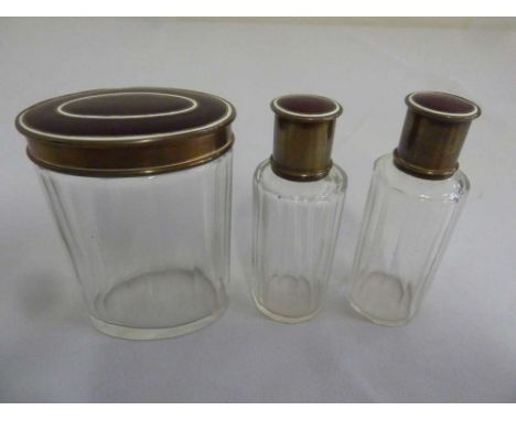 Three glass dressing table bottles with enamel and brass covers