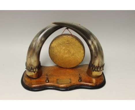 AN EARLY 20TH CENTURY SMALL DINNER GONG, the gong raised on two horn supports and a shaped oak base, bearing a presentation p