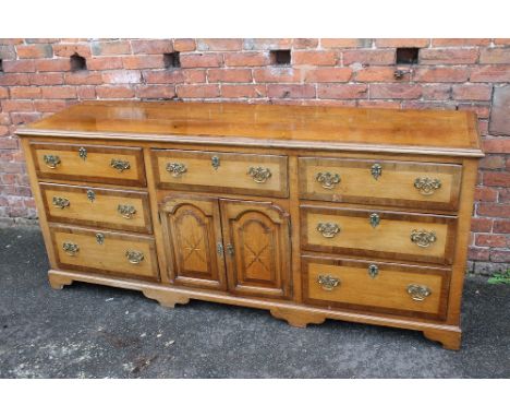 A GEORGE III OAK AND MAHOGANY DRESSER, the plank top with mahogany crossbanding, above an arrangement of seven drawers and ce