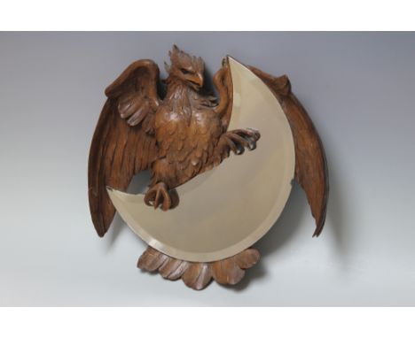 A LATE 19TH / EARLY 20TH CENTURY BLACK FOREST WALL MIRROR, carved in the form of an eagle holding a crescent shaped mirror, t
