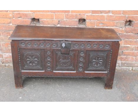 AN 18TH CENTURY OAK CARVED COFFER, the hinged lid above a three panel front, heavily carved with the original steel lock, rai