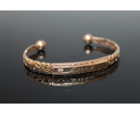 A 9 CARAT GOLD DIAMOND SET BANGLE, having a pierced acanthus swirl design either side of a central name plate set with a bril