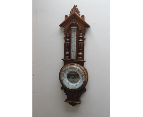 AN EARLY 20TH CENTURY OAK CARVED ANEROID BAROMETER, of Gothic style, carved with half turned columns, thermometer capsule to 