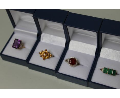 FOUR 9 CARAT GOLD DRESS RINGS CONSISTING OF A LARGE AMETHYST RING,  a fire opal ring, a three stone emerald ring and a yellow