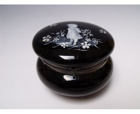 AN UNUSUAL BLACK GLASS LIDDED TRINKET WITH MARY GREGORY DECORATION, the hinged lid with metal mounts, Dia. 9 cm Buyers - for 