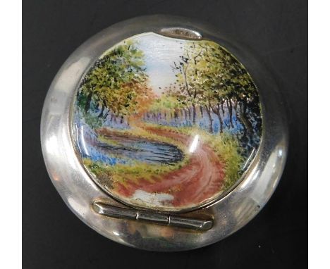 A silver and enamel circular pill box, with enamel panel of trees and river scene, (AF), 27.4g all in. 