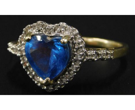 A heart shaped dress ring, the central blue stone heart surrounded by tiny white stones to border and shoulders, yellow metal