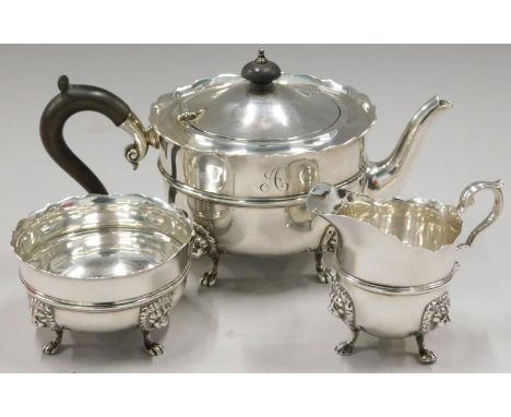 A George V silver three piece tea service, the teapot with ebonised knop and handle, on shaped legs headed by lion masks term