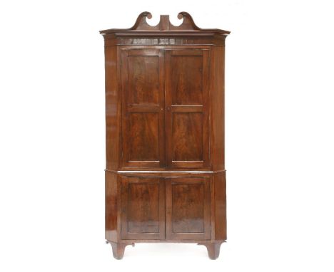 A George III mahogany standing corner cupboard,having a scrolled cornice over four panelled doors and bracket feet, the green