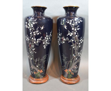 A Pair of Japanese Cloisonné Vases each decorated with birds amongst foliage upon a dark blue ground with hardwood stands, 29