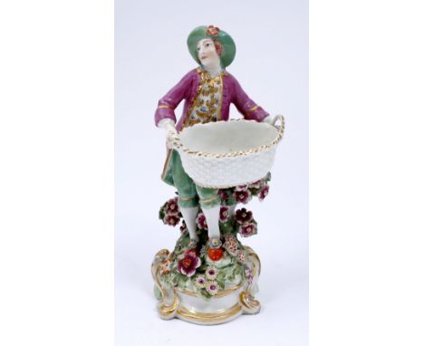 Chelsea porcelain sweetmeat figure circa 1765 wearing a green wide brimmed hat, pink jacket and green breeches, holding an ov