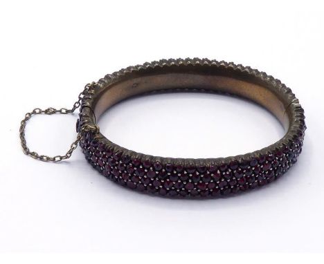 A 19th century Bohemian garnet bangle, composed of three rows of uniform rose cuts, mounted in pinchbeck, 58mm inner diameter