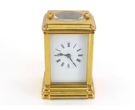 A brass-cased carriage clock with black Roman numerals on the white face, oval escapement view panel and hour/half hour strik