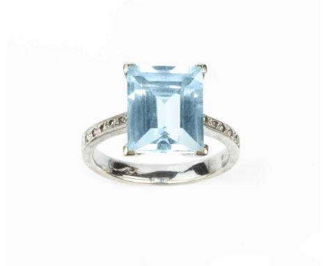 A blue topaz and diamond dress ring, the rectangular step-cut blue topaz in four claw setting, between tapered shoulders of s