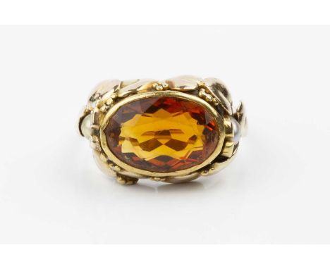 An Arts and Crafts style citrine and pearl dress ring, the oval mixed-cut citrine collet set within a border of stylized leav