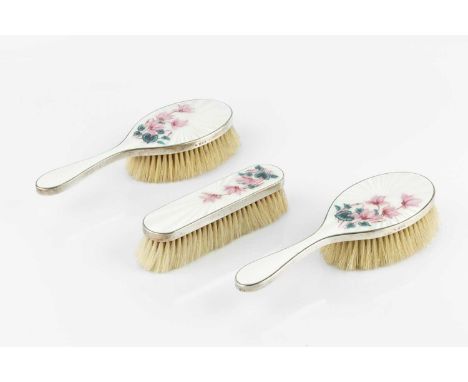 A pair of silver and enamel backed hair brushes, and a matching clothes brush, the ivory guilloche enamel backs painted with 