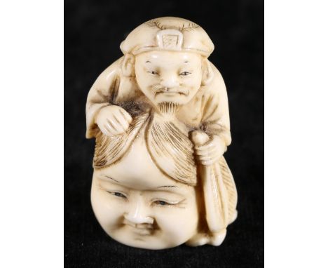 Japanese ivory netsuke of a man holding a large mask of Okame, 4cm Meiji