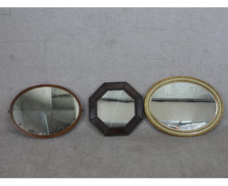 A collection of three wall mirrors, including an octagonal oak framed mirror, an oval mahogany framed mirror, and an oval pai