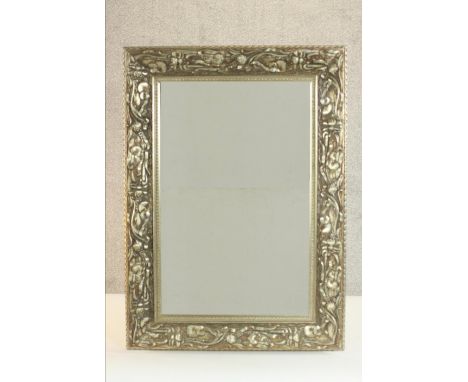 An Art Nouveau style carved and silvered pine mirror, with a rectangular bevelled mirrored plate, the frame decorated with st