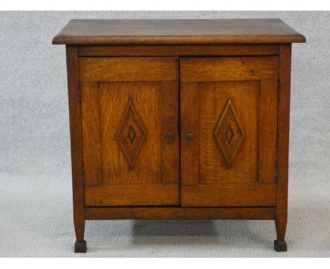 An early 20th century Arts and Crafts oak side cabinet with carved panel doors on squat square tapering supports on block fee