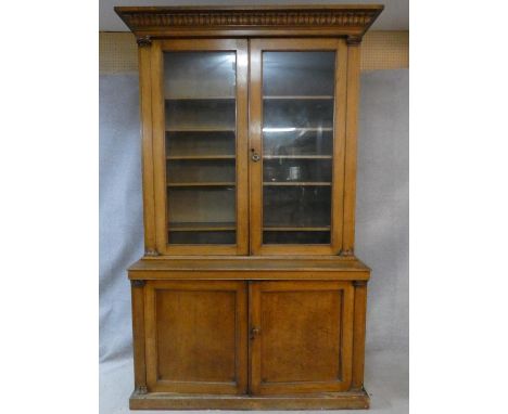 A mid 19th century oak library bookcase with acanthus carved pediment above glazed doors enclosing shelves flanked by Corinth