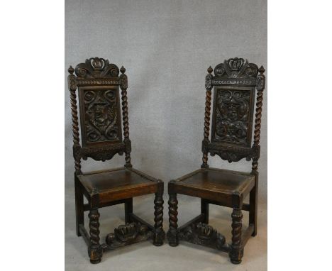 A pair of Continental antique oak hall chairs with crown crestings to the carved backs above panel seats on heavy barleytwist
