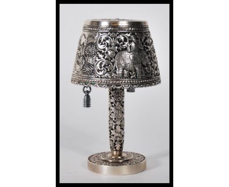 A 20th Century silver/ white metal table lighter in the form of table lamp, having decorative repousse shade depicting Indian
