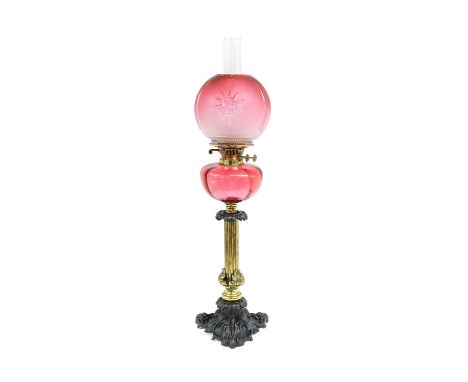 A Gilt and Patinated Metal and Cranberry Glass Oil Lamp, the globe shade with star burst decoration on a panelled reservoir, 