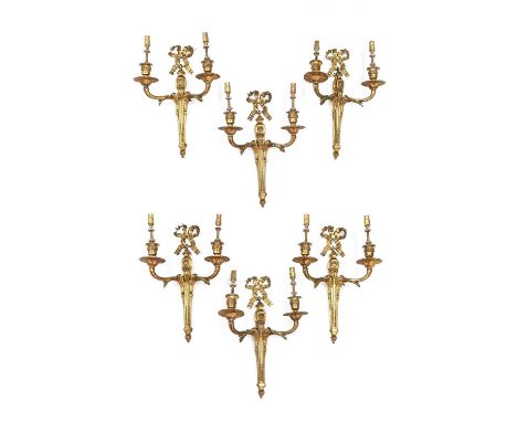 A Set of Six Gilt Metal Twin-Light Wall Sconces, in Louis XVI style, with ribbon-tied cresting over volute scroll backplates 