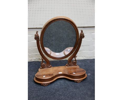 A Victorian mahogany toilet mirror, the cushion framed oval plate within swept scrolled horns on a twin lidded concave base a