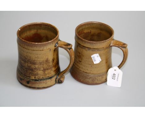 Two similar Leach pottery tankards with capped scroll handles and tapering bodies, bearing impressed marks to base, the highe