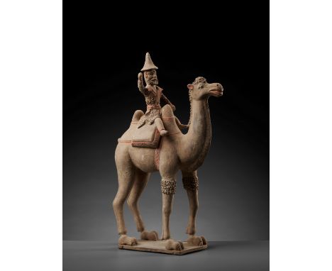 A LARGE PAINTED POTTERY BACTRIAN CAMEL WITH RIDER, TANG DYNASTYChina, 618-907. The two-hump camel standing foursquare on a re