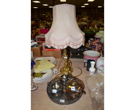 A three-piece plated tea service on a circular plated salver; and a brass table lamp with pink shade.